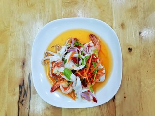 Thai food style, Top view of spicy Thai seafood salad on white plate on wooden table in restaurant, This food is most popular, Yum Talay is Thai traditional