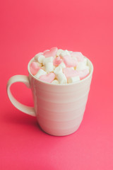 Mug with marshmallows in the shape of heart on pink background