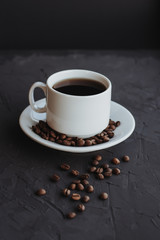 White cup of coffee and coffee beans on a dark background