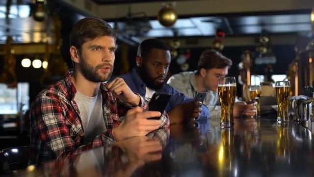 Anxious man checking bets on cellphone, watching sports in bar, bookmaker app