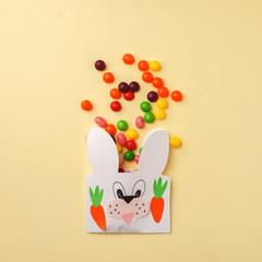 Easter colorful candy and Jellybean flowing from party paper handcraft bag on yellow white background. Easter bunny package. copy space, flat lay, Happy Easter concept