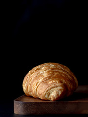 Croissant with icing on wood board in Chiaroscuro photo style, black background.