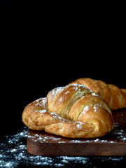 Croissant with icing on wood board in Chiaroscuro photo style, black background.