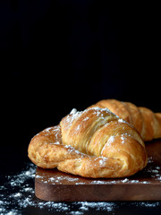 Croissant with icing on wood board in Chiaroscuro photo style, black background.