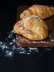 Croissant with icing on wood board in Chiaroscuro photo style, black background.