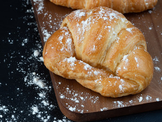 Croissant with icing on wood board in Chiaroscuro photo style, black background.