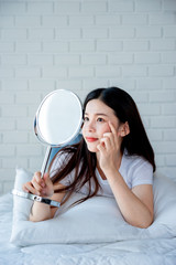 Asian teenage woman  looking at mirror and squeeze acne problem on her face, skin care concept.