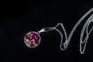 Resin pendant with dry rose petals on a dark background close up