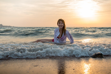 Fototapeta na wymiar Girl rests and has fun in sea wave at sunset