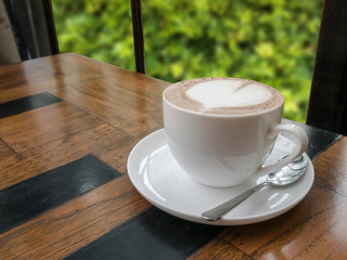 close up of a cup of hot chocolate with heart on wood table,blur tree background