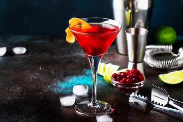 Classic alcoholic cocktail cosmopolitan with vodka, liqueur, cranberry juice, lime, ice and orange zest, dark bar counter background, night mood, space for text - obrazy, fototapety, plakaty