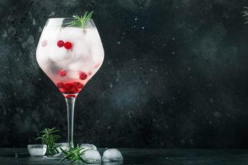 Cranberry cocktail with ice, rosemary and berries in big wine glass, bar tools, gray bar counter...
