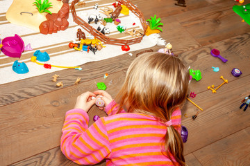 Little girl child playing with lots of colorful plastic toys on wooden floor indoors