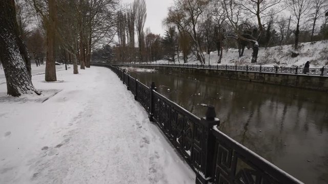 Walking along river embankment with metal railing in winter city park steadicam gimbal movement.