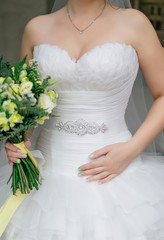 Bride in white wedding dress with green and yellow bouquet, showing her belt decorated with crystals