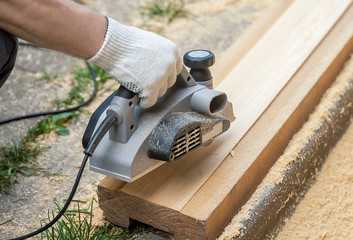 The hand of a man working with electric planers outdoor. Shavings debris ejected from the machine. Handle with right hand. Processing of material. Work tool. Woodworking and craftsmanship concept