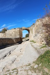 Obraz premium The central street of the cavecity Chufut-Kale. Above the road is visible arch, left from the gate in the fortified wall. It's a medieval city-fortress in the Crimean Mountains that now lies in ruins.