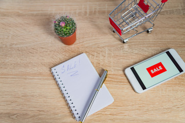 close up view of office desk with white smartphone with sale text, note and small shopping cart. Technology business online shopping concept
