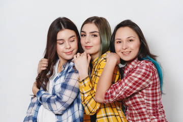 Three stylish girls best friends. Standing together and having fun. Looking at camera. On gray background.