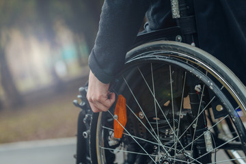 Naklejka premium Close-up of male hand on wheel of wheelchair during walk in park