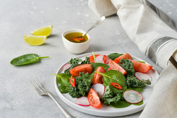 fresh salad of organic spinach, kale, tomatoes and radish with olive oil and lime juice. healthy eating concept. diet, vegan cuisine. light background, selective focus