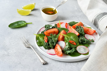 fresh salad of organic spinach, kale, tomatoes and radish with olive oil and lime juice. healthy eating concept. diet, vegan cuisine. light background, selective focus