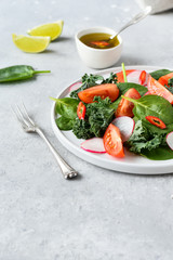 fresh salad of organic spinach, kale, tomatoes and radish with olive oil and lime juice. healthy eating concept. diet, vegan cuisine. light background, selective focus