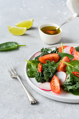 fresh salad of organic spinach, kale, tomatoes and radish with olive oil and lime juice. healthy eating concept. diet, vegan cuisine. light background, selective focus