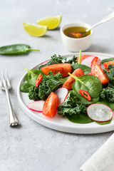 fresh salad of organic spinach, kale, tomatoes and radish with olive oil and lime juice. healthy eating concept. diet, vegan cuisine. light background, selective focus