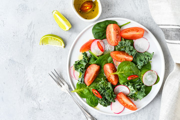 fresh salad of organic spinach, kale, tomatoes and radish with olive oil and lime juice. healthy eating concept. diet, vegan cuisine. light background, selective focus