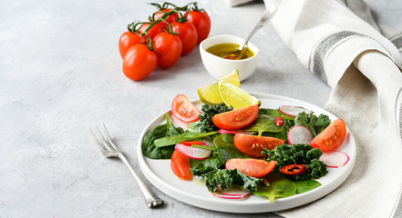 fresh salad of organic spinach, kale, tomatoes and radish with olive oil and lime juice. healthy eating concept. diet, vegan cuisine. light background, selective focus