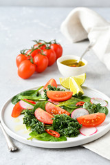 fresh salad of organic spinach, kale, tomatoes and radish with olive oil and lime juice. healthy eating concept. diet, vegan cuisine. light background, selective focus
