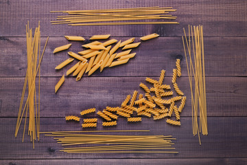 Dry Italian pasta - fusilli, spaghetti and penne. Variety of types and shapes of uncooked italian macaroni on wooden background.