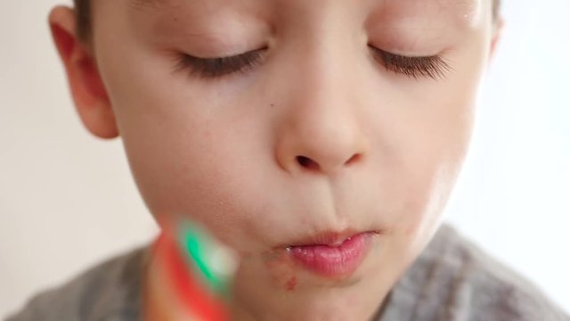 Portrait of a child of preschool age. A cute, little boy opens his mouth and eats a lady, candy, close-up.