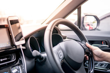 Male driver hand holding on steering wheel using smartphone for GPS navigation. Mobile phone mounting with magnet on the car console in modern car. Urban driving lifestyle with mobile app technology