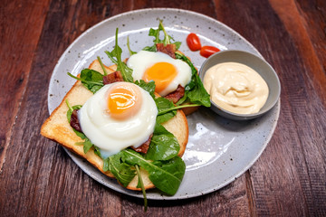 Breakfast sandwich with eggs, bacon and sour cream in a plate on wooden table
