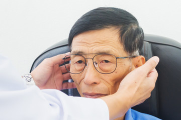 Optician male hands put glasses on elderly man testing his eye, ophthalmology concept.