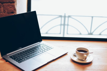 Open laptop and a Cup of coffee on the table in the cafe, freelance concept
