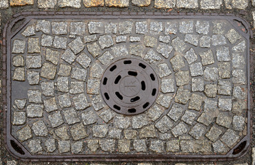 Old metal manhole cover on cobblestone street, Jelenia Gora,  Poland