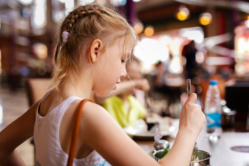 Blonde girl in white and blue dress having lunch in the restaurant