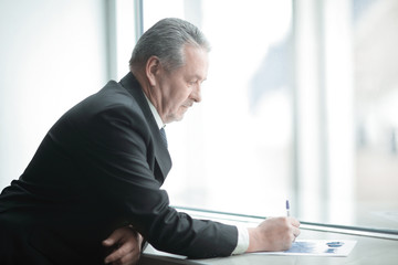 Fototapeta premium businessman signs a document, standing near the office window