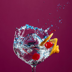 Cocktail in glass with splashes garnished with lemon and cherries.