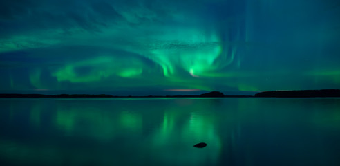 Northern lights dancing over calm lake in Farnebofjarden national park in Sweden.