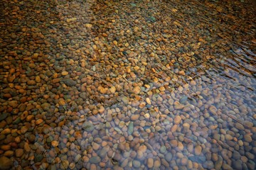 Abstract nature background of colorful pebbles stones under lake or river, copy space. Wet pebble rocks on beautiful island beach, vintage style. Top view of rocky sea stones texture in sun light. 