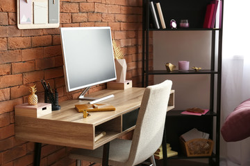 Workplace with modern computer and golden decor near brick wall in room