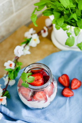 Colorful fruit salad in a jar on white and blue rustic wooden background.top view. Strawberry milkshake in jar with flowers