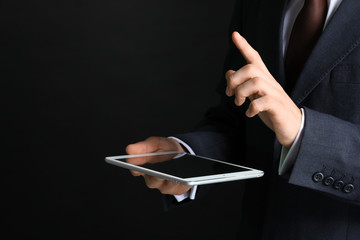 Businessman with tablet computer using virtual screen on dark background