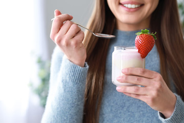 Young woman eating tasty yogurt at home, closeup