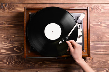 Woman switching on record player with vinyl disc on wooden background