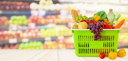 Shopping basket filled with fruits and vegetables on wood table with supermarket grocery store blurred defocused background with bokeh light